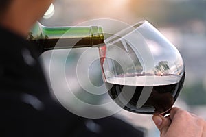 Young man`s hand poured red wine into a glass of wine at a restaurant in a romantic atmosphere. Sunset and modern city background