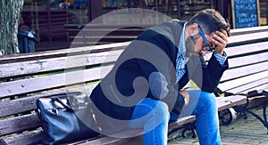 Young man with sad facial expression sitting on a bench in the park. Office worker lost his job. Middle aged man despair