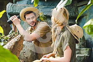 young man in safari suit with parrot on shoulder flirting with woman while hiking