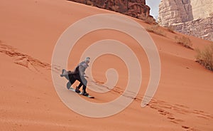 Young man sand dune surfing wearing bisht - traditional Bedouin coat. Sandsurfing is one of the attractions in Wadi Rum desert photo