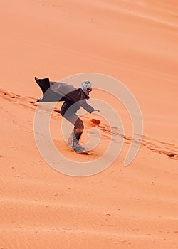 Young man sand dune surfing wearing bisht - traditional Bedouin coat. Sandsurfing is one of the attractions in Wadi Rum desert