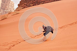 Young man sand dune surfing wearing bisht - traditional Bedouin coat. Sandsurfing is one of the attractions in Wadi Rum desert photo