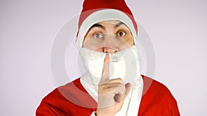 Young man in santa claus suit holding finger on his lips over white background.