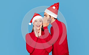 Young Man In Santa Hat Whispering Christmas Secret To His Excited Girlfriend