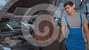 Young man with sarcastic facial expression listening woman walking to open car hood gesturing in slow motion. Portrait