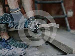 A young man is sawing a board with an electric saw.