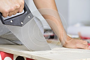 Young man sawing a wooden board with a handsaw