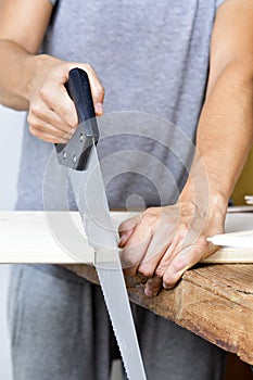 Young man sawing a wooden board with a handsaw