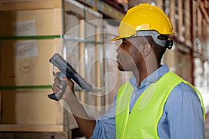 Young man scanning a barcode working in a warehouse. African man wearing helmet and reflective jacket working in a warehouse.