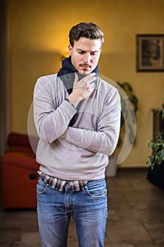 Young man with scarf, holding his neck because of throat ache