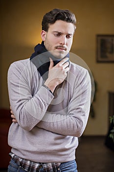 Young man with scarf, holding his neck because of throat ache