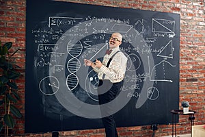 Young man, scientist, lecturer standing by blackboard with math and scientific formulas, making calculations