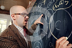 Young man, scientist standing by blackboard with formulas and calculations. Chemistry lessons