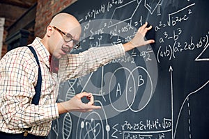 Young man, scientist standing at blackboard with formulas and calculations, thinking, counting in mind. Math