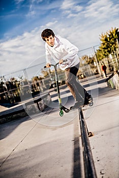 Young man with scooter making a Grind on Skatepark