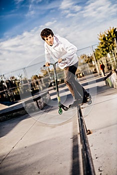 Young man with scooter making a Grind on Skatepark photo