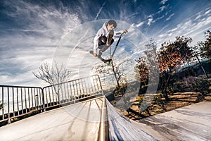 Young man with scooter making a jump on Skatepark during sunset