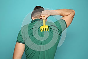 Young man scratching back with toy rake on color background.