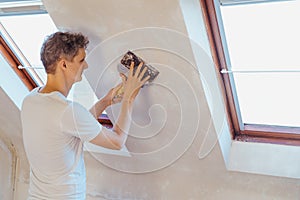 A young man scratching with a spatula and removing old wallpaper on a wall of a room. Do it yourself concept. Home photo