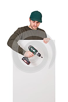 Young man with a screwdriver or electric drill in his hand, stands behind a white panel. Renovation worker before installing