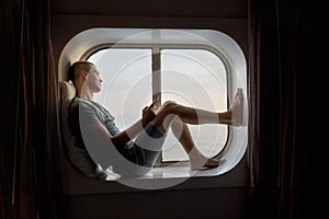 Young man seated in front of a porthole reading a digital book