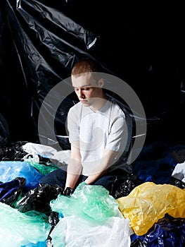 Young man seated on plastic bag garbage, environmental - consciousness concept, shoot inside in studio