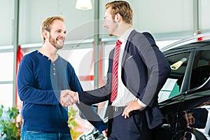 Young man and seller with auto in car dealership