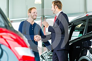 Young man and seller with auto in car dealership photo