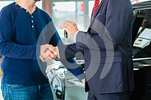 Young man and seller with auto in car dealership photo