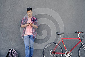 Young man sending a text while standing with his bike