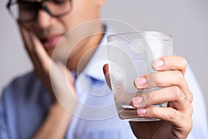 Young man with sensitive teeth and hand holding glass of cold water with ice. Healthcare concept