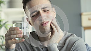 Young man with sensitive teeth and hand holding glass of water