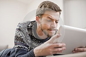 Young man looking at a tablet computer while lying on the couch.