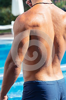 Young man With Sexy Body In Swimwear around Swimming Pool Water At Relax Spa Resort. Fitness Model With Skin Sun Tan Relaxing On