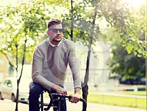 Young man in shades riding bicycle on city street