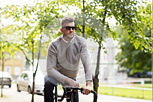 Young man in shades riding bicycle on city street