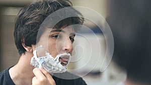 Young man shaving beard in front of mirror