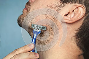 Young man without shaving cream on his face, grooming his beard with straight razor,