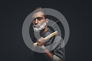 Young man with shaving cream on his face, holding an axe and looking