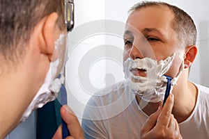 Young man shaving in front of a mirror in the bathroom. Skin care concept