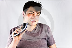 A young man shaving his chin with an electric shaver. Teenager holding his electric trimmer. Handsome young man is using an electr