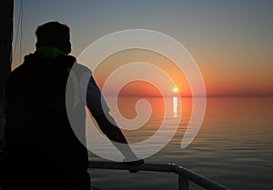 Young man on a ship during a cruise enjoys the sunrise