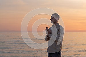 young man in a shirt, making a prayer in a sunset on the beach