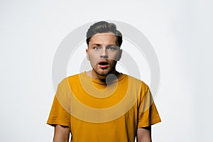 Young man shocked looking at camera wearing yellow t-shirt isolated on white background. Human face expressions