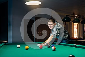 Young man shooting ball in billiard by cue