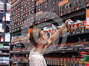 Young man shopping and choosing hinges from shelves in a hardware store warehouse