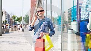 Young man shopping in the mall with many colored shopping bags in his hand. He is holding a phone.