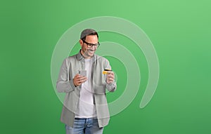 Young man shopping online with phone and making mobile payment with credit card on green background