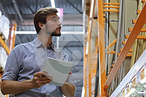 Young man shopping or working in a hardware warehouse standing checking supplies on his tablet