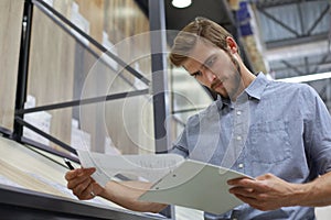 Young man shopping or working in a hardware warehouse standing checking supplies on his tablet